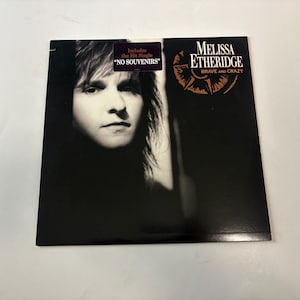 Pode incluir: Capa do álbum "Brave and Crazy" de Melissa Etheridge. A arte do álbum apresenta um retrato em preto e branco de Etheridge, com o título do álbum e um design de rosa dos ventos. Um adesivo diz "Includes the Hit Single 'No Souvenirs'".