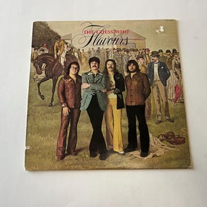 以下が含まれることがあります： ザ・ゲス・フーのヴィンテージ・レコード・アルバムのカバー。カバーアートは、馬とライダーを背景に、フィールドにいるバンドメンバーを描いています。アルバムのタイトル「ザ・ゲス・フー・フレーバーズ」は、大きくスタイリッシュな文字で印刷されています。