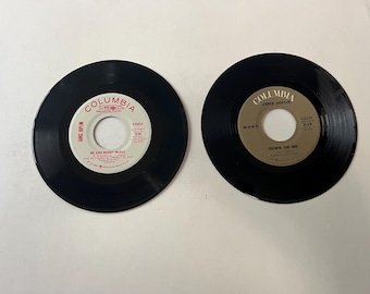 May include: Two black vinyl records with white labels. The record on the left has the text "Columbia" and "He And Bobby McGee" on the label. The record on the right has the text "Columbia" and "Down On Me" on the label.