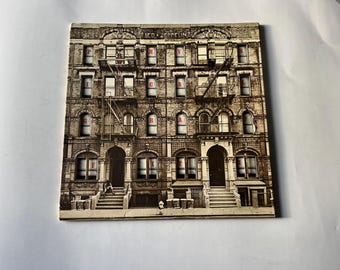 May include: Album cover featuring a sepia-toned photograph of a brick apartment building with fire escapes. The word "PHYSICAL GRAFFITI" is spelled out in red letters in the windows. The band name "LED ZEPPELIN" is at the top.