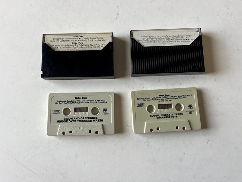 May include: Two cassette tapes, one labeled "Simon and Garfunkel Bridge Over Troubled Water" and the other labeled "Blood, Sweat & Tears Greatest Hits".