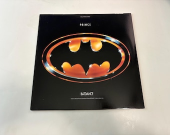 Puede incluir: Portada de álbum de vinilo de "Batdance" de Prince, de la banda sonora de la película Batman. La portada es negra con un gran logotipo de Batman estilizado en naranja y dorado. El nombre del artista, "PRINCE", está en la parte superior, y "BATDANCE" debajo del logotipo.