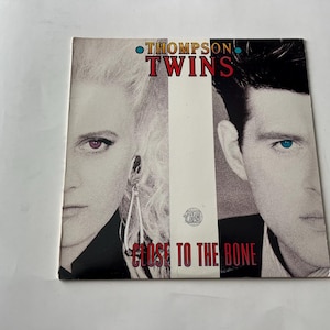 May include: A black and white album cover with a photo of two people. The album is titled "Thompson Twins" and the album title is "Close to the Bone".