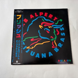Puede incluir: Portada de &aacute;lbum de vinilo para Herb Alpert's Tijuana Brass, con una colorida ilustraci&oacute;n de un toro sobre un fondo negro. El t&iacute;tulo del &aacute;lbum y el nombre del artista est&aacute;n en colores vibrantes. Texto japon&eacute;s a la izquierda.