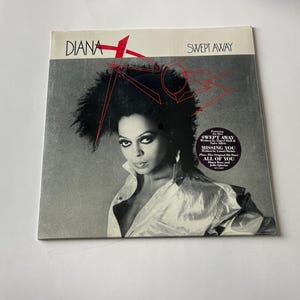 May include: A black and white vinyl record cover featuring a woman with short, curly black hair. The cover is titled "Diana" and "Swept Away". The album features the songs "Swept Away", "Missing You", and "All Of You".