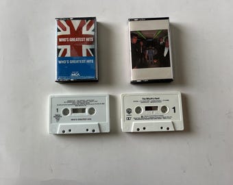 May include: Two cassette tapes, one with a white label and the text "The Who's Hard" and the other with a white label and the text "Who's Greatest Hits". The cassette tapes are on a white surface.