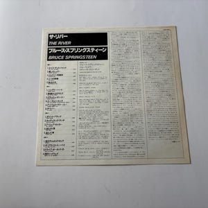 May include: A vintage album cover for Bruce Springsteen's "The River." The cover features Japanese text and English titles, including "THE RIVER" and "BRUCE SPRINGSTEEN." The album's tracklist is also visible. The cover is on a white background.