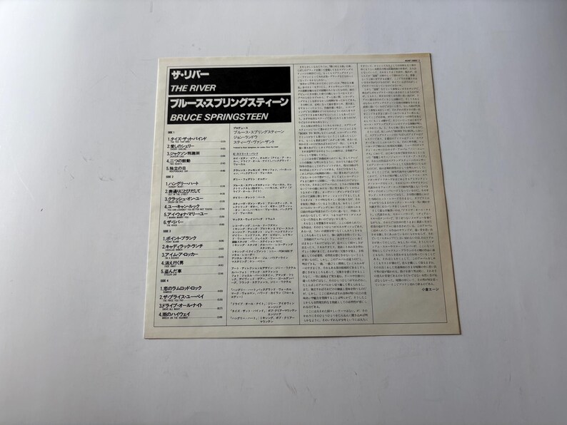 May include: A vintage album cover for Bruce Springsteen's "The River." The cover features Japanese text and English titles, including "THE RIVER" and "BRUCE SPRINGSTEEN." The album's tracklist is also visible. The cover is on a white background.