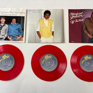 May include: A collection of Michael Jackson album covers and red vinyl records. Album covers include "Thriller", "Off The Wall", and "The Girl Is Mine". The records are red with yellow and silver labels.