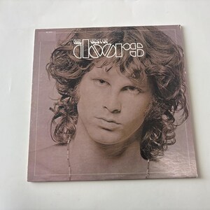 May include: A square vinyl record cover featuring a sepia-toned portrait of Jim Morrison with long wavy hair. The text at the top reads The Best of The Doors in a white stylized font. The album cover has a thin white border frame.