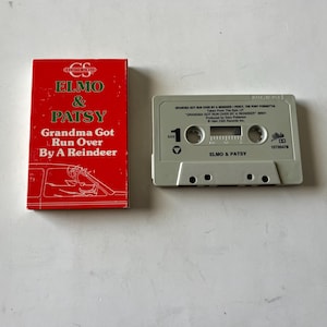 May include: A red cassette tape case with the title "Grandma Got Run Over By A Reindeer" by Elmo & Patsy. The cassette tape is white with the title "Elmo & Patsy" and the song title "Grandma Got Run Over By A Reindeer".