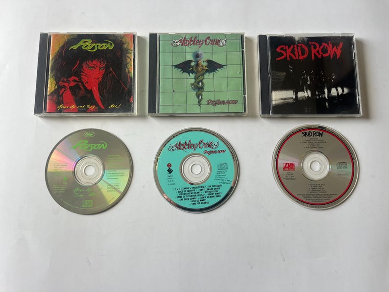 May include: Three compact disc cases with the band names "Poison", "Motley Crue", and "Skid Row" printed on the front. The cases are black with silver trim. The CDs are silver with the band names printed on them.