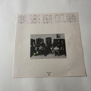 May include: A vintage album cover featuring a black and white photograph of a band in a room. Above the photo are stylized letter designs. The album cover is on a white background.