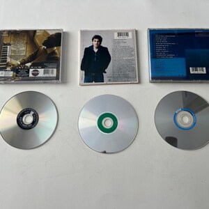 Puede incluir: Se muestran tres discos compactos y sus estuches. Los estuches muestran ilustraciones y texto. Los CD son plateados con centros de colores. Los estuches son rectangulares y transparentes, con ilustraciones visibles.