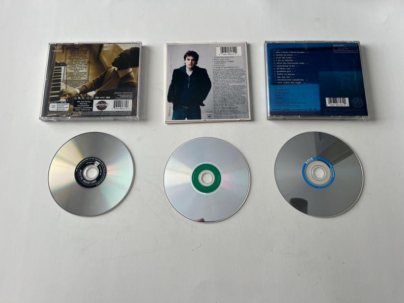 Puede incluir: Se muestran tres discos compactos y sus estuches. Los estuches muestran ilustraciones y texto. Los CD son plateados con centros de colores. Los estuches son rectangulares y transparentes, con ilustraciones visibles.
