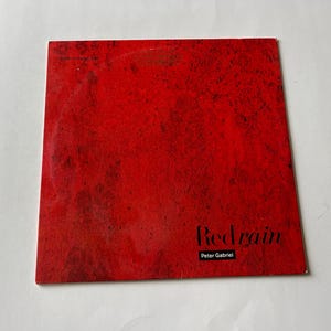 May include: Red vinyl record album cover with a red background and the text "Red Rain" in black with the artist "Peter Gabriel" in smaller black text below.