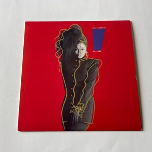 May include: A red album cover with a woman in a black outfit outlined in gold. The album cover has the text "Janet Jackson" and "Control" on it.