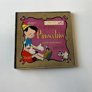 May include: A vintage record album cover featuring a cartoon image of Pinocchio from Walt Disney's Pinocchio. The cover is a light pink color with a gold frame and features the title "Walt Disney's Pinocchio" in large, bold letters. The album is by RCA Victor and conducted by Cliff Edwards.