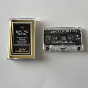 以下が含まれることがあります： 「Electric Blues Gold Collection」と題された白黒のラベルが付いたカセットテープ。エルモア・ジェームス、B.B.キング、マディ・ウォーターズ、ハウリン・ウルフ、そしてソニー・ボーイ・ウィリアムソンなど、アーティストの名前が記載されています。カセットテープは透明なプラスチックケースに入っています。