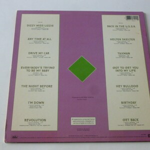 Op de afbeelding: De achterkant van een roze vinyl platenalbum met een groene diamant in het midden. Het album is getiteld "The Beatles" en bevat een lijst met nummers, waaronder "Dizzy Miss Lizzie", "Any Time At All", "Drive My Car", "Everybody's Trying To Be My Baby", "The Night Before", "I'm Down", "Revolution", "Back In The U.S.S.R.", "Helter Skelter", "Taxman", "Got To Get You Into My Life", "Hey Bulldog", "Birthday" en "Get Back".