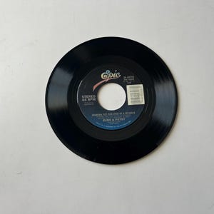 May include: A black 45 RPM vinyl record with a white label. The label has the text "Epic" in a blue and white logo, "STEREO 45 RPM", "GRANDMA GOT RUN OVER BY A REINDEER" and "ELMO & PATSY".