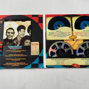 May include: A red, white, and blue themed Rock 'n' Roll Anniversary box set with a black and white checkered background. The box set includes a DVD, a trivia quiz, and a booklet with facts about Rock 'n' Roll. The front of the box features a photo of three musicians.