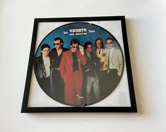 Disco de vinilo con imagen de Huey Lewis & The News en marco negro (1984)