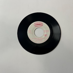 May include: A black vinyl record with a white label. The label has red text that reads "Grandma Got Run Over By A Reindeer" by Elmo & Patsy. The label also has the text "Soundwaves" in red.