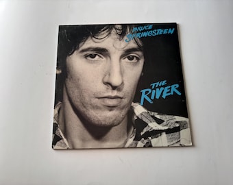 May include: Album cover for "The River" by Bruce Springsteen. The cover features a black and white portrait of Springsteen with the album title and artist name in blue text. The background is black.