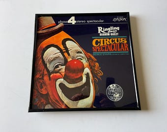 Può includere: Una copertina di un album di vinile vintage con un clown sorridente con un naso rosso e un costume colorato. L'album è intitolato "Ringling Bros. Barnum & Bailey Circus Spectacular" con il testo "Phase 4 Stereo Spectacular" e "The Greatest Show on Earth" stampato sulla copertina.
