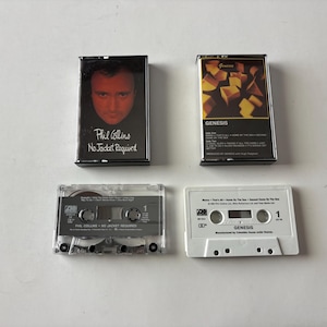May include: Two music cassette tapes with their respective plastic cases. One case features Phil Collins No Jacket Required with a portrait, while the other shows the Genesis album cover with abstract yellow shapes on a black background.