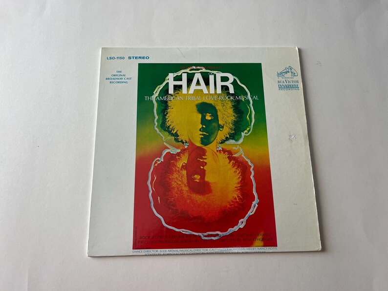 May include: A vintage vinyl record album cover for the musical "Hair: The American Tribal Love-Rock Musical". The cover features a psychedelic design with a person's face surrounded by a colorful, swirling pattern.