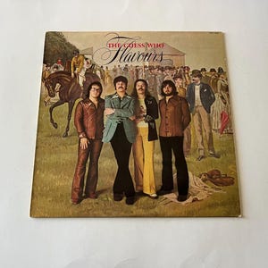 以下が含まれることがあります： 「ザ・ゲス・フー」というバンドの、ヴィンテージのビニールレコードアルバムのカバーで、アルバムのタイトルは「フレーバーズ」です。カバーアートは、1970年代の服装をした男性グループが、馬とライダーを背景に、フィールドに立っている様子を描いています。