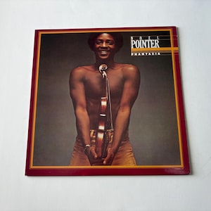 May include: Album cover featuring Noel Pointer, with the title "Phantazia." The cover has a red and gold border. Pointer is shirtless, holding a violin. The background is a gradient of gray and brown.