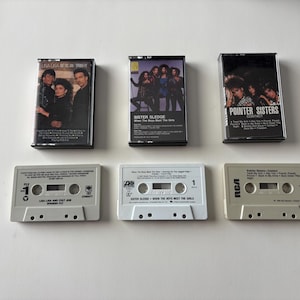 May include: Six vintage cassette tapes are displayed against a white background. Three are in black cases with album art, featuring Lisa Lisa and Cult Jam, Sister Sledge, and Pointer Sisters. The other three are the cassette tapes themselves, in light gray and white.