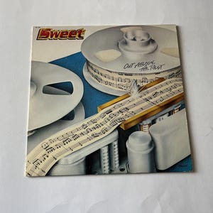 May include: A vintage vinyl record album cover featuring the band Sweet. The album cover is a close-up of a reel-to-reel tape recorder with music sheets. The album title is "Cut Above The Rest".