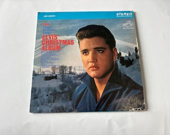 May include: A vintage vinyl record cover for Elvis' Christmas Album featuring a portrait of Elvis Presley in a blue collared shirt against a snowy mountain landscape. The text includes the album title, tracklist, and the RCA Victor logo.