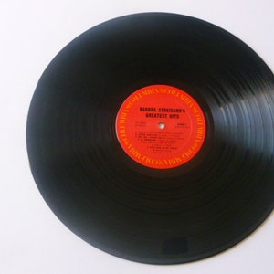 May include: Black vinyl record with a red and orange label that reads "Barbra Streisand's Greatest Hits".
