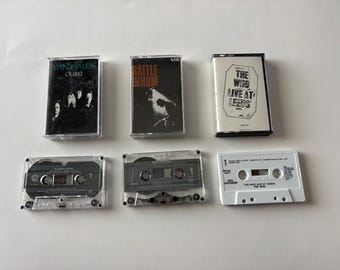 May include: Six vintage cassette tapes featuring album art from Van Halen, U2, and The Who. The tapes are in clear plastic cases, with the album titles and band names printed on the covers. The tapes are arranged on a white surface.