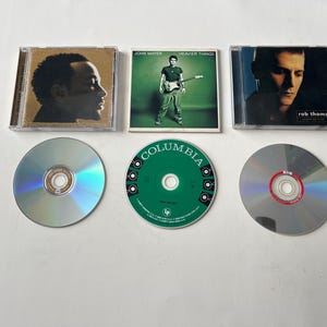 Puede incluir: Tres CD con estuches y discos. Los estuches de CD presentan portadas de &aacute;lbumes de John Mayer, Rob Thomas y otro artista. Los discos son plateados y verdes. El CD de John Mayer est&aacute; etiquetado como "Heavier Things".