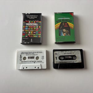 Könnte beinhalten: Vier Vintage-Kassetten mit Albumcovern von Bob Marley & The Wailers. Die Kassetten enthalten die Alben "Survival" und "Hot-Line" mit farbenfrohen Grafiken und Text. Die Kassetten sind schwarz, weiß und grün.