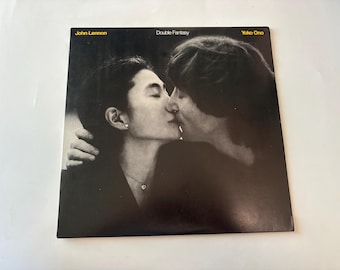 May include: A square vinyl record cover for the album Double Fantasy by John Lennon and Yoko Ono. The cover features a black and white photograph of the two individuals kissing, with the text John Lennon, Double Fantasy, and Yoko Ono in yellow.