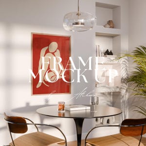 May include: A framed art print with a red background and a white abstract figure is displayed on a white wall. The text "FRAME MOCK UP" is overlaid on the image. A round black table with two chairs and a glass pendant light are in the foreground.