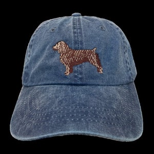 May include: A blue denim baseball cap with an embroidered brown and white dog silhouette.