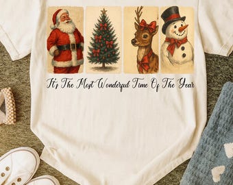 Könnte beinhalten: Cremefarbenes T-Shirt mit weihnachtlichen Illustrationen von Santa Claus, einem Weihnachtsbaum, einem Rentier und einem Schneemann. Der Text "It's The Most Wonderful Time Of The Year" ist unter den Bildern aufgedruckt.