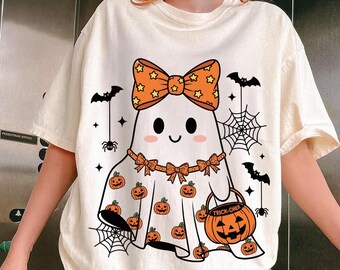 May include: Cream-coloured Halloween-themed t-shirt featuring a friendly ghost character with a bow, pumpkin accents, and a trick-or-treat bag. The design includes bats, spiders, and spiderwebs, creating a festive and playful look.