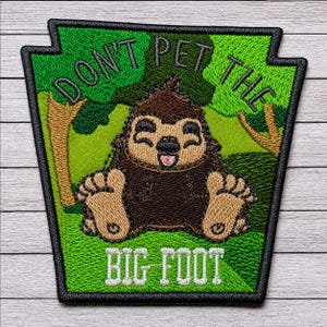 Op de afbeelding: Een trapeziumvormige geborduurde patch met een bruin Bigfoot-figuur in een groene bosrijke omgeving. De tekst DON'T PET THE is in het zwart bovenaan geborduurd en BIG FOOT in het wit onderaan. De patch heeft een zwarte rand.
