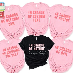 a collection of pink t-shirts with various humorous text printed on them, along with a black t-shirt featuring a different text message.