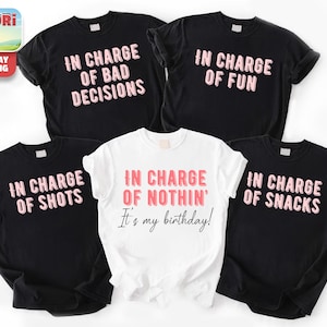 a collection of five t-shirts, each with a unique phrase printed on it. The phrases include "In charge of bad decisions", "In charge of fun", "In charge of nothing", "It's my birthday!", and "In charge of snacks". The t-shirts are arranged in a row, showcasing the variety of messages and styles.