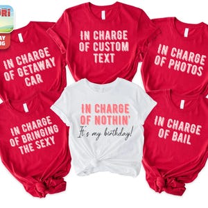 a collection of red t-shirts with white text, arranged in a row. The text on the t-shirts reads "In charge of getting away from the car, in charge of custom text, in charge of photos, in charge of bailing, in charge of bringing the Sexy, in charge of my birthday!" The t-shirts are arranged in a row, with the white t-shirt in the center.